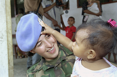 Una peacekeeper delle Nazioni Unite tiene in braccio una bambina che gioca, attirata dal suo cappello, Timor Est.
