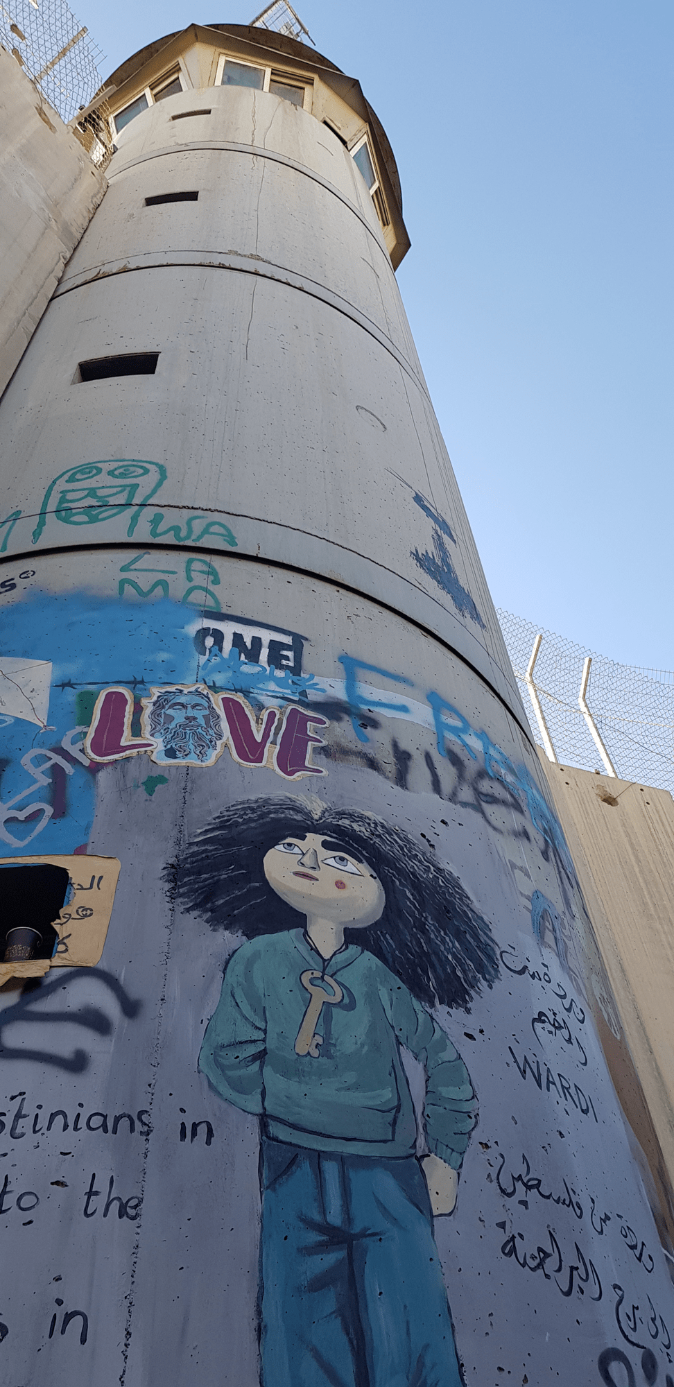 The challenge of human rights in Palestine, University of Padova, 17 May 2023. 
An Israeli control tower along the wall dividing Israel and the West Bank. On the tower is a mural of a little girl with a key around her neck looking up.
