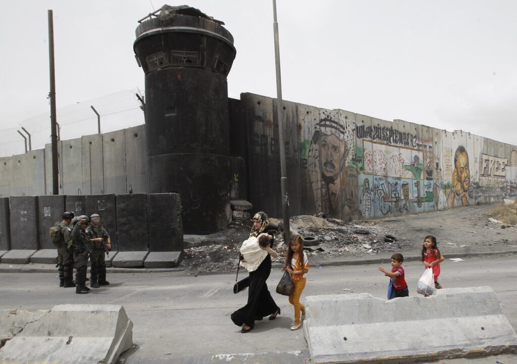 Una donna palestinese e dei bambini camminano davanti alle forze israeliane di guardia davanti al checkpoint di Qalandia, vicino alla città cisgiordana di Ramallah il 5 giugno 2014 