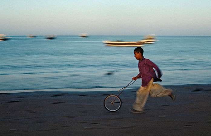 Immagine di un bambino che gioca con una ruota di bicicletta lungo la spiaggia in Iran