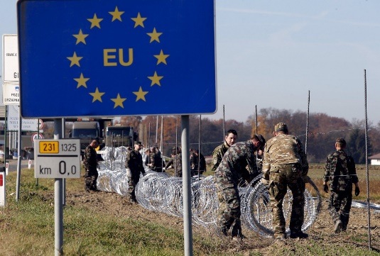 soldiers are closing the border with barbed wire, under an EU sign 
