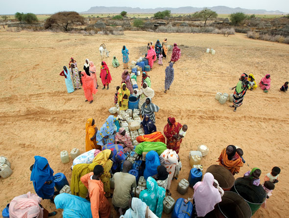 Gruppo di donne in abiti colorati al punto di distribuzione dell'acqua nel Nord Darfur. La fonte d'acqua più vicina si trova ad una distanza di un'ora e mezza; gli asini sono di solito usati per il trasporto dell'acqua al villaggio.  