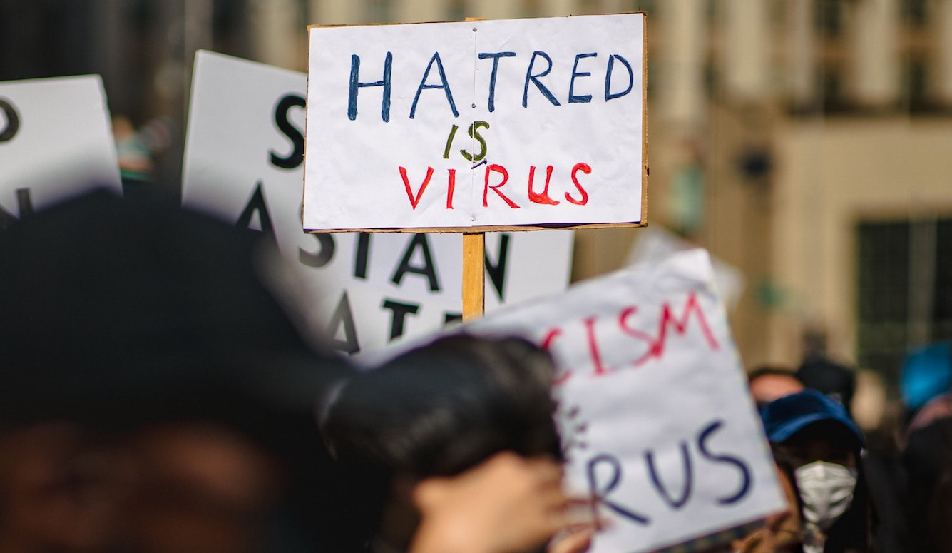 A poster help up during a protest that says "hatred is virus"