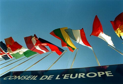 Fotografia di un'insegna con la scritta "Conseil de l'Europe" con delle bandiere sovrastanti di alcuni degli stati membri.
