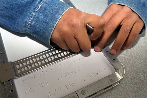 Primo piano di due mani di un bambino mentre scrivono in Braille con l'ausilio di una tavola tattile.