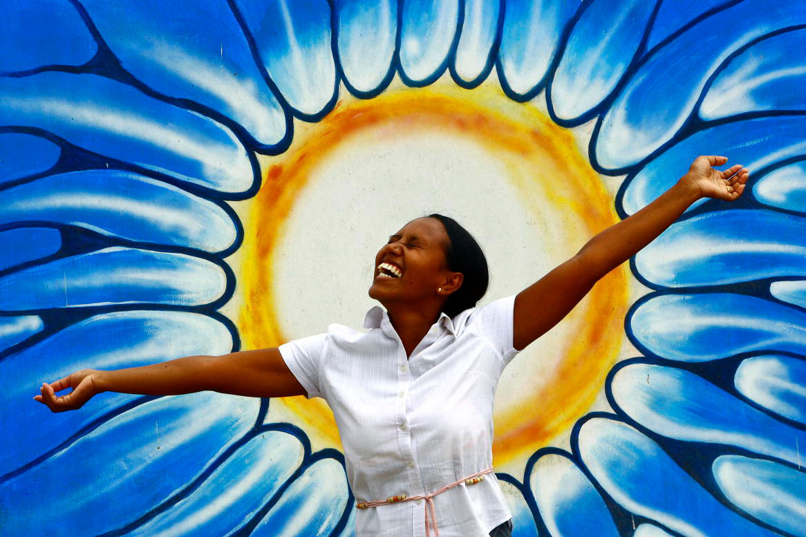 Una donna posa di fronte ad un graffito che rappresenta un Sole