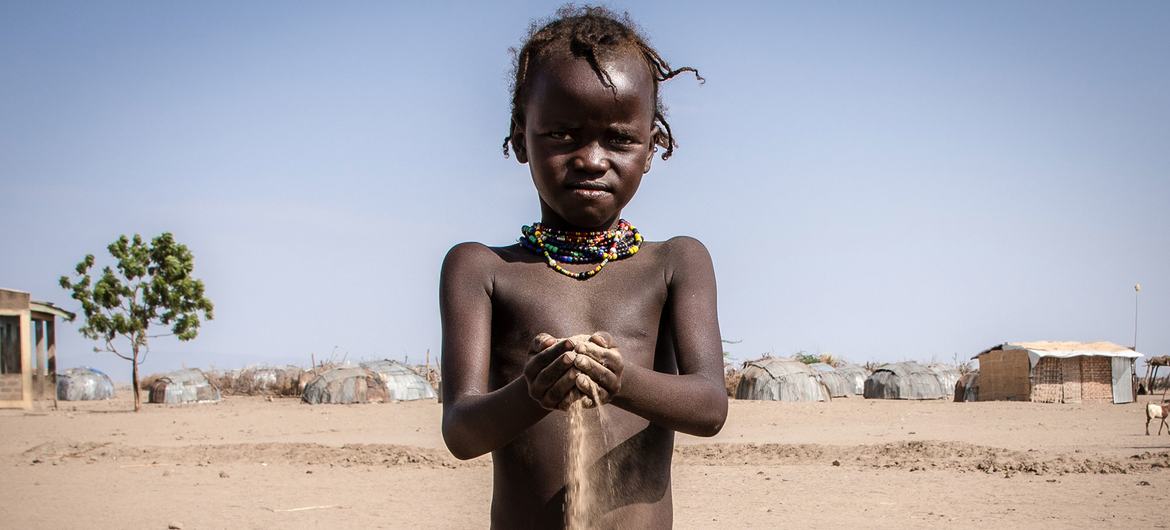 Bambino africano tiene in mano la sabbia del deserto. Villaggio sullo sfondo. 
