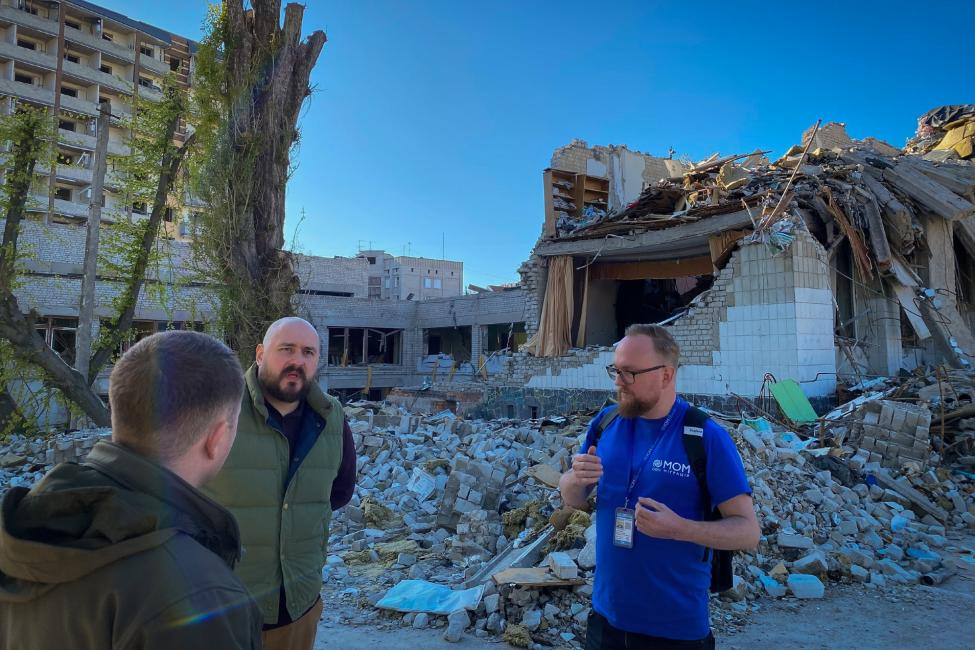 IOM staff and local authorities discuss the needs of internally displaced persons in front of a damaged school in Zhytomyr centre.