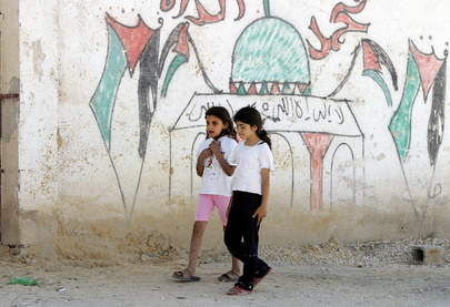 Due ragazzine passeggiano nel campo profughi palestinese di Acqba Jaber gestito dall'Agenzia delle Nazioni Unite per il Soccorso e l'Occupazione, accanto ad un muro su cui è raffigurata una moschea riportante i colori palestinesi.
