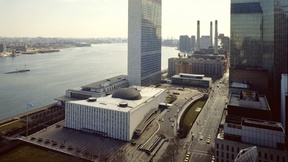 Aerial view of the United Nations Headquarters. Two low rectangular buildings and a skyscraper, overlooking the Hudson River in New York.