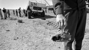 Incidente in un campo minato: in primo piano una mano che sorregge una scarpa dilaniata e sullo sfondo il veicolo dell'ONU coinvolto.