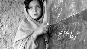 Foto in bianco e nero di una bambina ritratta in piedi di fronte alla lavagna di una scuola dell'UNICEF.