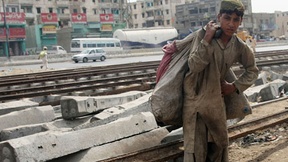 Ragazzo pakistano con umili vestiti mentre lavora in prossimità delle rotaie del treno a Karachi.