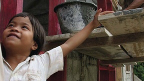 Copertina del Rapporto annuale 2008 di UN-HABITAT, programma delle Nazioni Unite per gli insediamenti umani. Nella foto un bambino sorridente in primo piano ed alle sue spalle un uomo che lavora su una impalcatura di un cantiere edile.