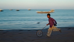 Immagine di un bambino che gioca con una ruota di bicicletta lungo la spiaggia in Iran