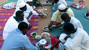 Celebrazione del Ramadan nel villaggio di El Fashir, Nord Darfur. Un gruppo di persone siede attorno ad una stuoia dove sono posti piatti e vivande.  