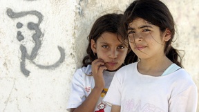 Due bambine registrate dall'Agenzia delle Nazioni Unite per il Soccorso e l'Occupazione (UNRWA) posano nel campo profughi di Acqba Jaber, nelle vicinanze di Jericho, accanto ad un muro con graffiti in arabo.