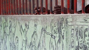 Un prigioniero afferra le sbarre di un muro esterno al penitenziario su cui è stato dipinto un murales di prigionieri.