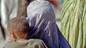 Una donna afgana, vestita con un burqa integrale, sorregge il proprio figlio all'interno del campo profughi Roghani a Chaman, una città al confine con il Pakistan