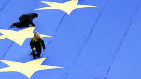 Particolare con quattro bambini appoggiati su 4 delle 12 stelle di una grande bandiera dell'Unione Europea