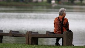 Una donna anziana siede da sola su una panchina vicino a uno stagno in Thailandia.