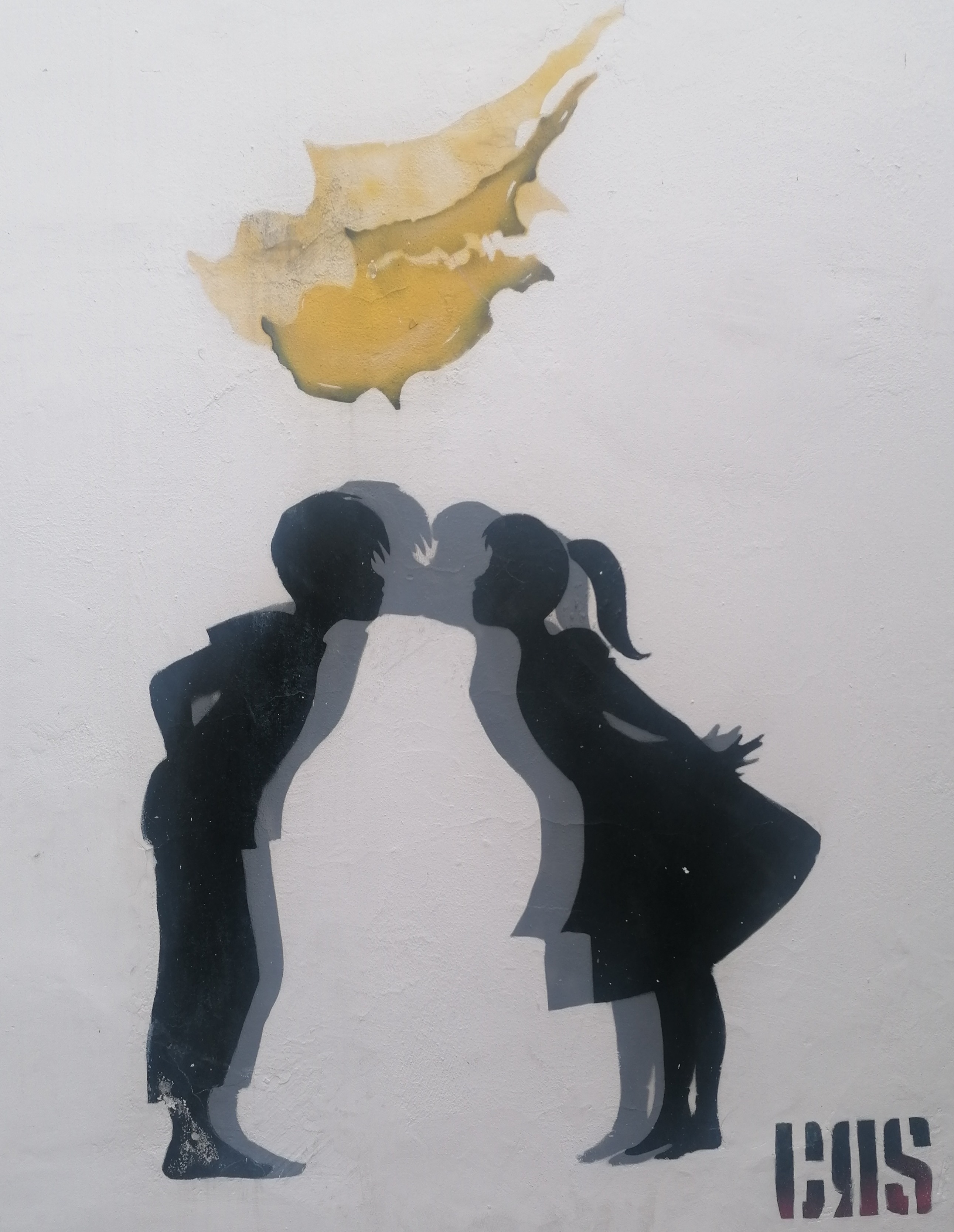 A painting of two children reaching for a kiss, their shadows actually kissing. Above them is a divided Cyprus, while the shadow is actually united.