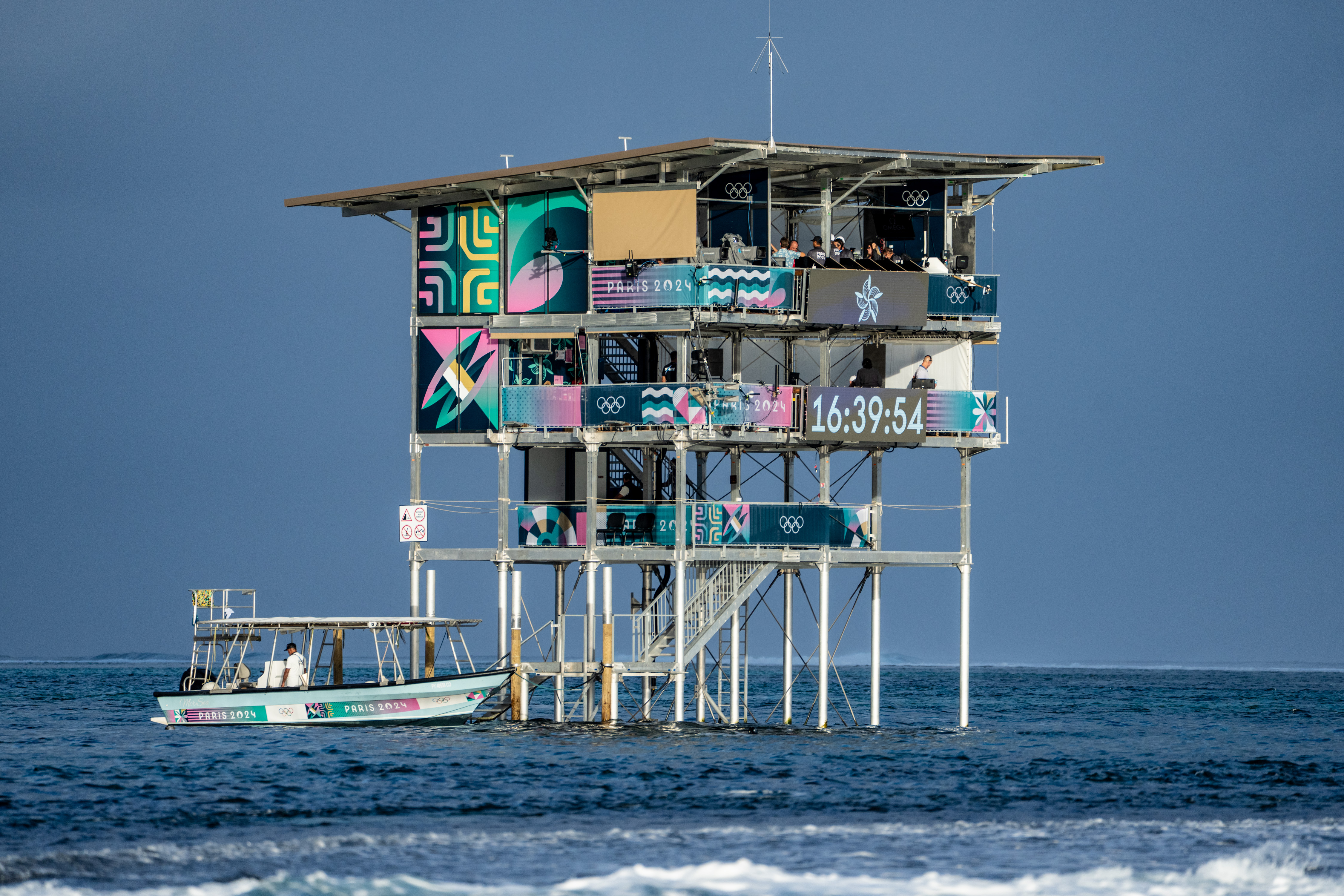 Scattata dal fotografo di surf di fama mondiale Tim McKenna, questa immagine costituisce una testimonianza visiva dell'intreccio tra lo sport globale e l'ecologia locale. La torre, pur essendo un capolavoro di ingegneria moderna progettato per la trasmissione delle Olimpiadi del 2024, si erge come un monolite controverso nel fragile «Mana» delle acque tahitiane. Rappresenta la dimensione visibile di una lotta ambientale invisibile, segnando il punto esatto in cui le tradizionali strutture in legno sono state sostituite dall'intervento industriale.